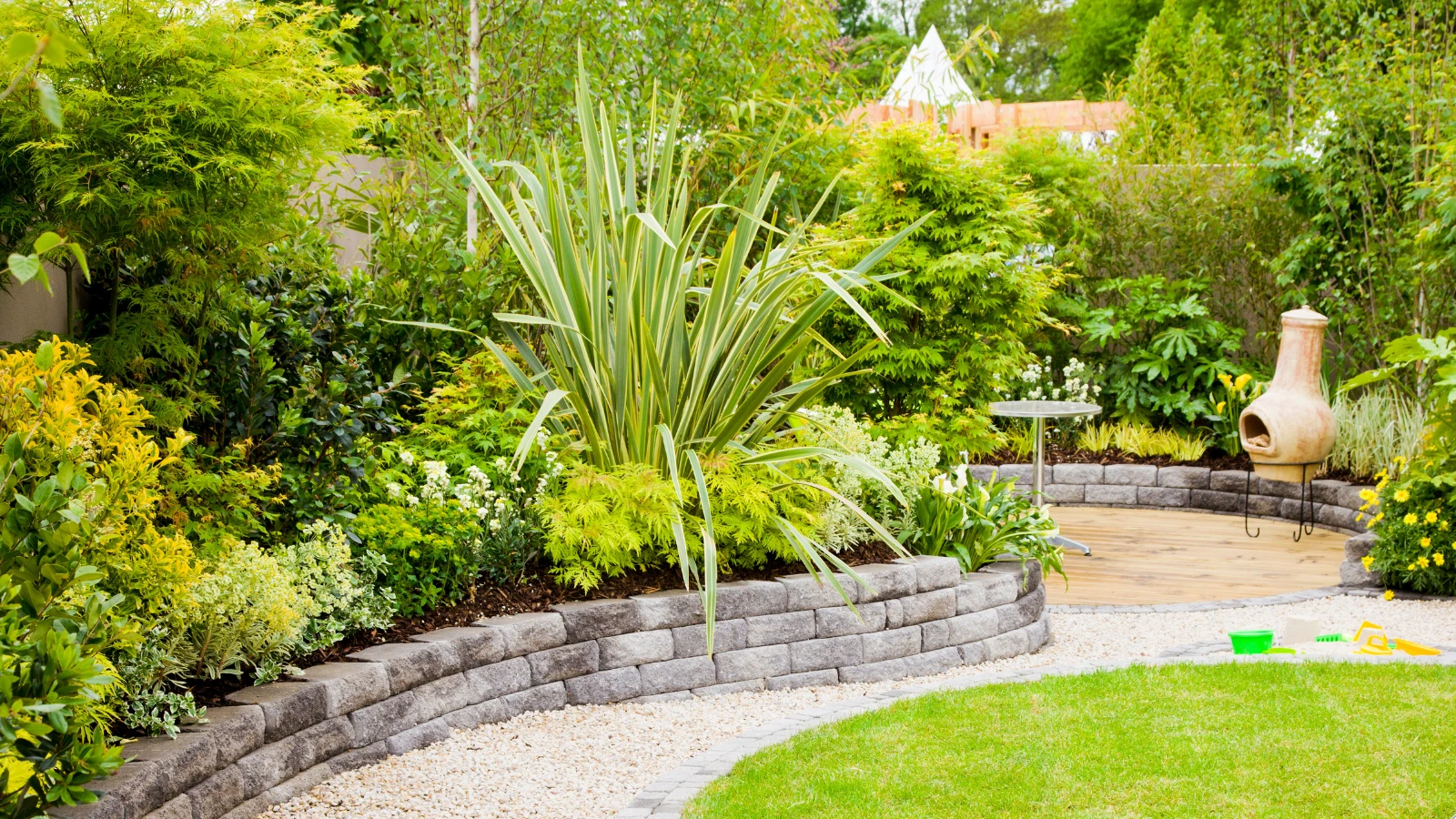 Lush backyard landscaping in Austin with stone retaining walls, colorful plants, and a wooden patio area for outdoor living.