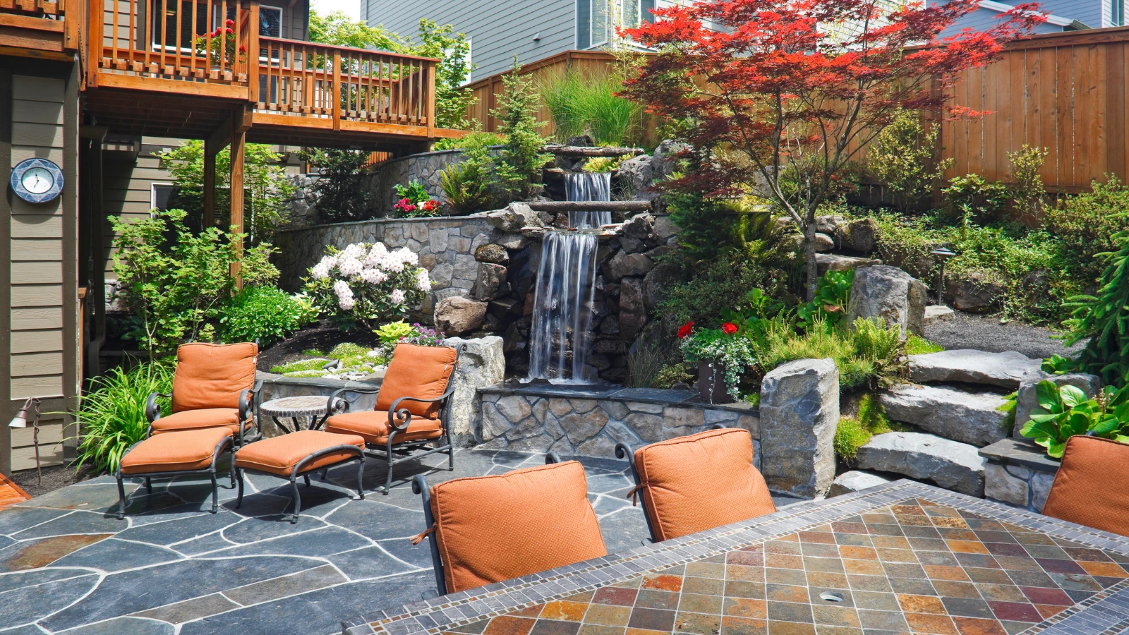 Stunning backyard with a waterfall, patio, stone features, and lush plants, illustrating a perfect blend of hardscaping vs landscaping.